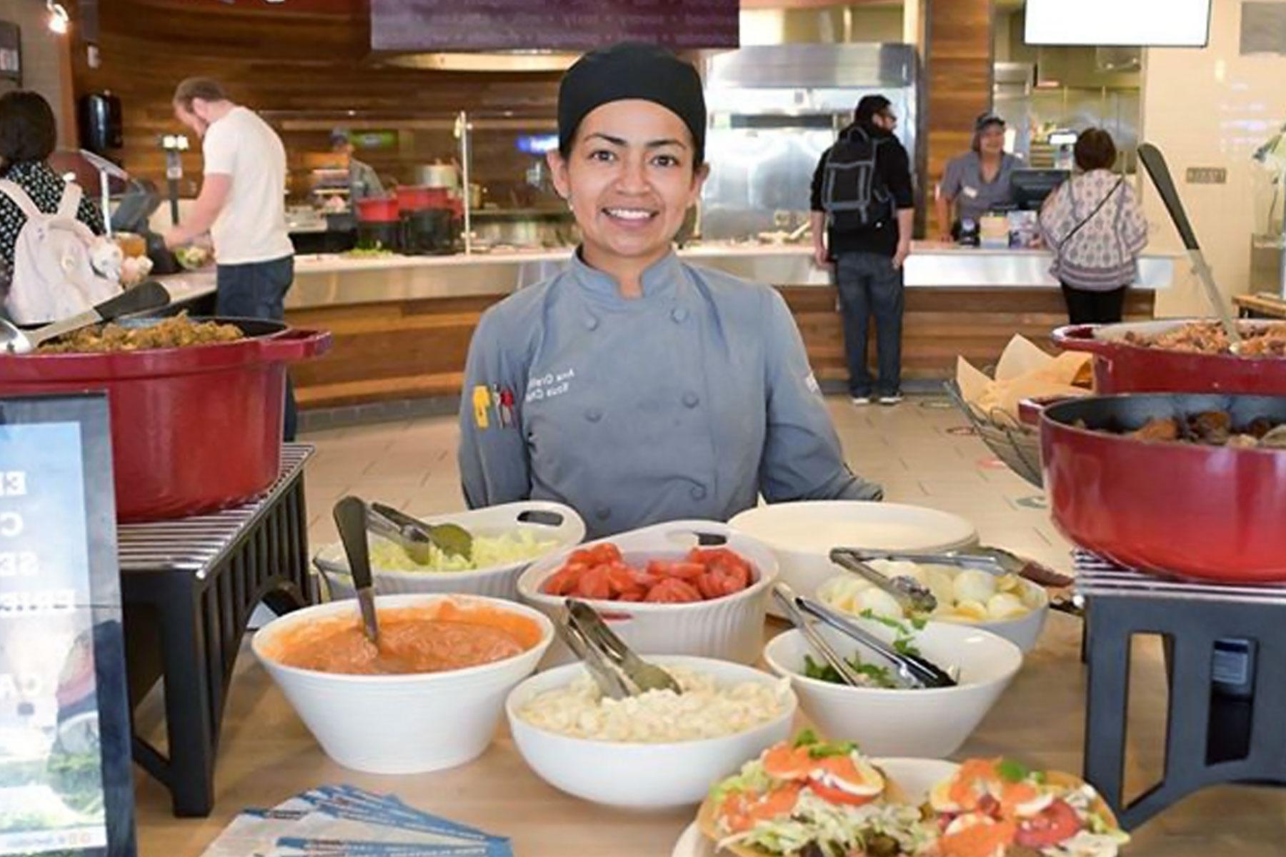 Female server behind a table of food options.